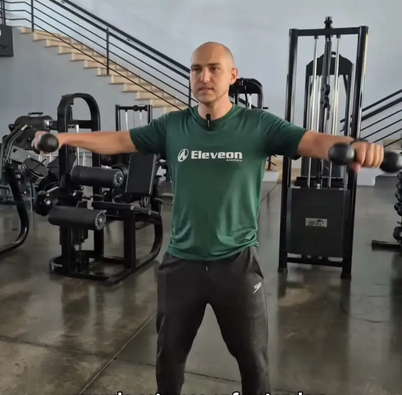 Professor da Eleveon fazendo elevação lateral com halteres na sala de musculação