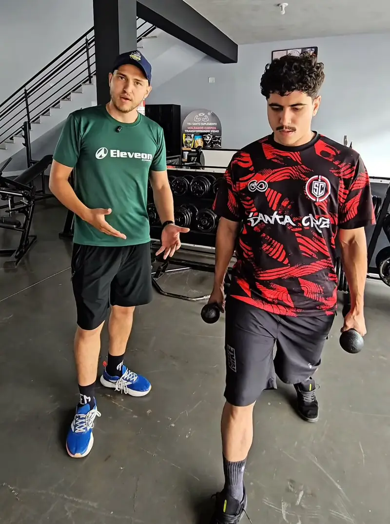 Professor da Eleveon orientando um aluno com halteres na sala de musculação